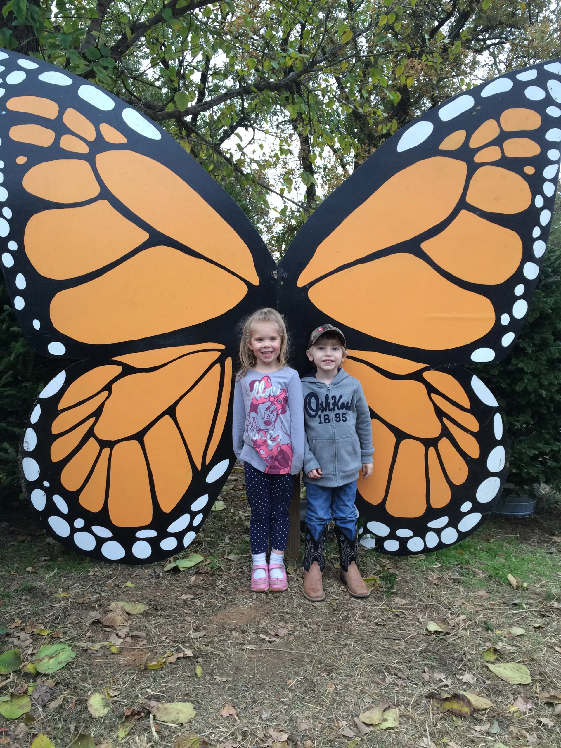Two kids posing in front of a giant butterfly for a professional photograph picture.