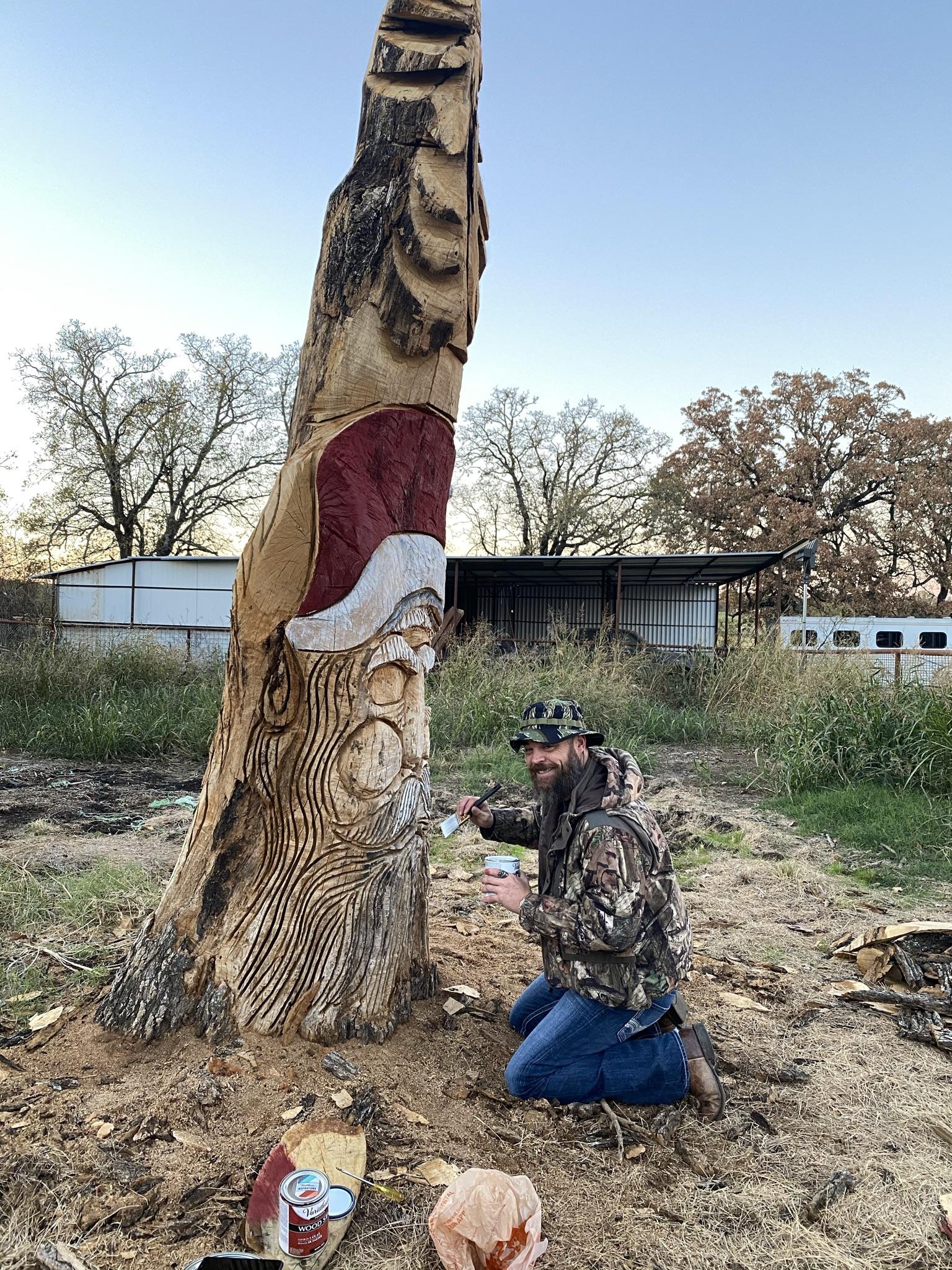 A man painting on a carved Santa in an old tree for the Christmas tree season at Haynie's Green Acres Christmas tree farm
